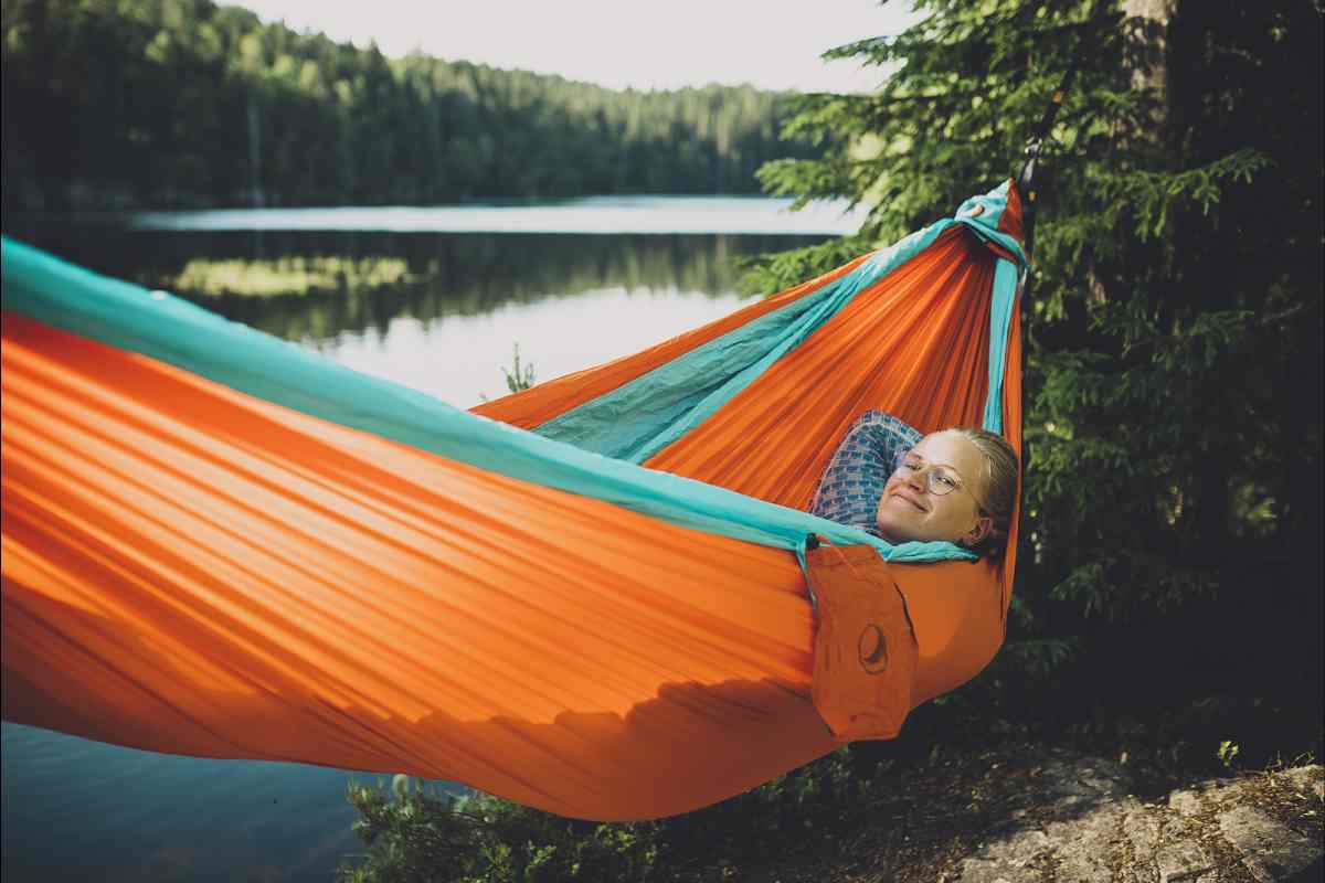 Una ragazza felice su un'amaca arancione e dietro un lago