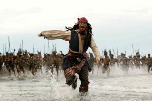 Un pirata di nome Jack Sparrow che corre in spiaggia con dietro una tribù
