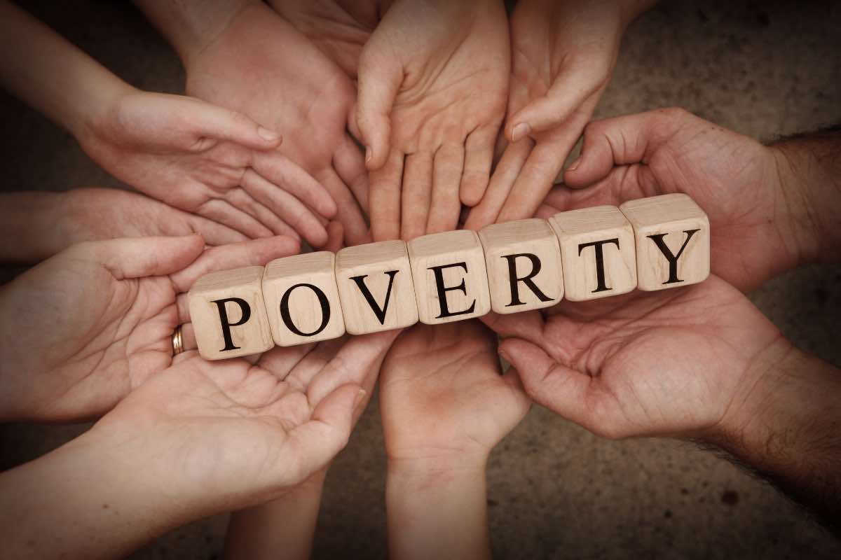 Scritta povertà in inglese appoggiata su tante mani