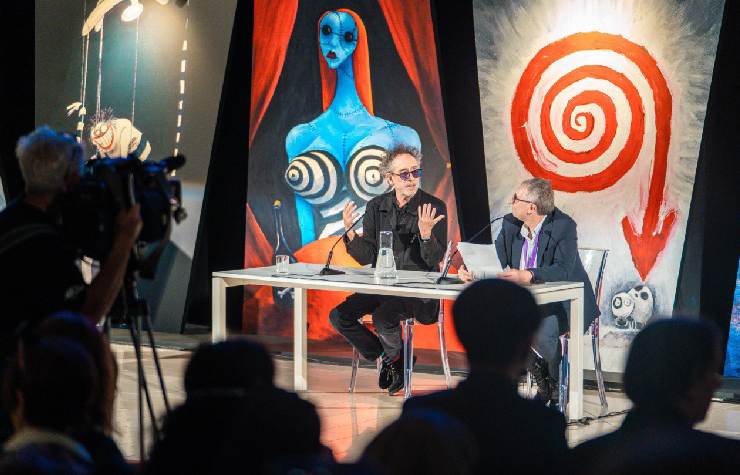 Tim Burton ad una conferenza con dietro i suoi disegni